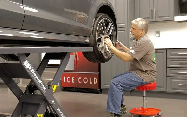 BendPak MDS-6LPF 6,000 lb. Capacity Mid-Rise Scissor Lift showing a mechanic polishing a wheel with a vehicle raised up on the bendpak scissor lift.
