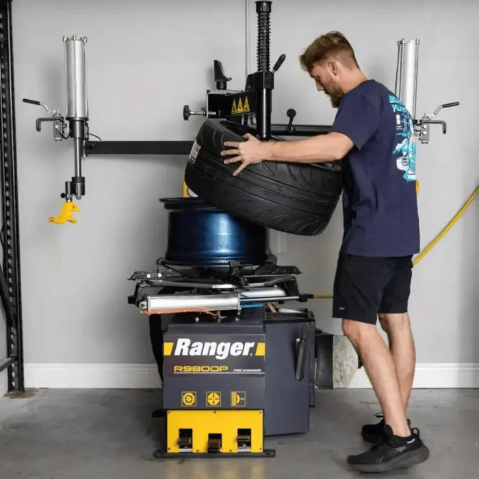 Ranger R980DP-L Tire Changer Swing Arm Dual-Tower Assist shown in a tire shop with a technician putting a tire onto a wheel - Mechanic Super Store